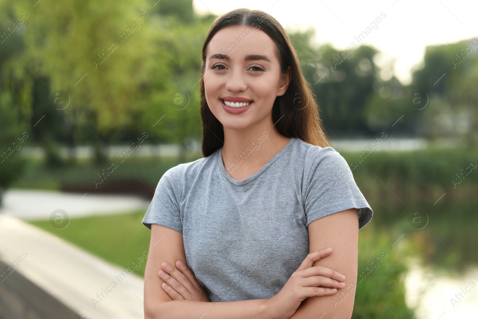 Photo of Portrait of beautiful woman with crossed arms outdoors. Attractive lady smiling and looking into camera