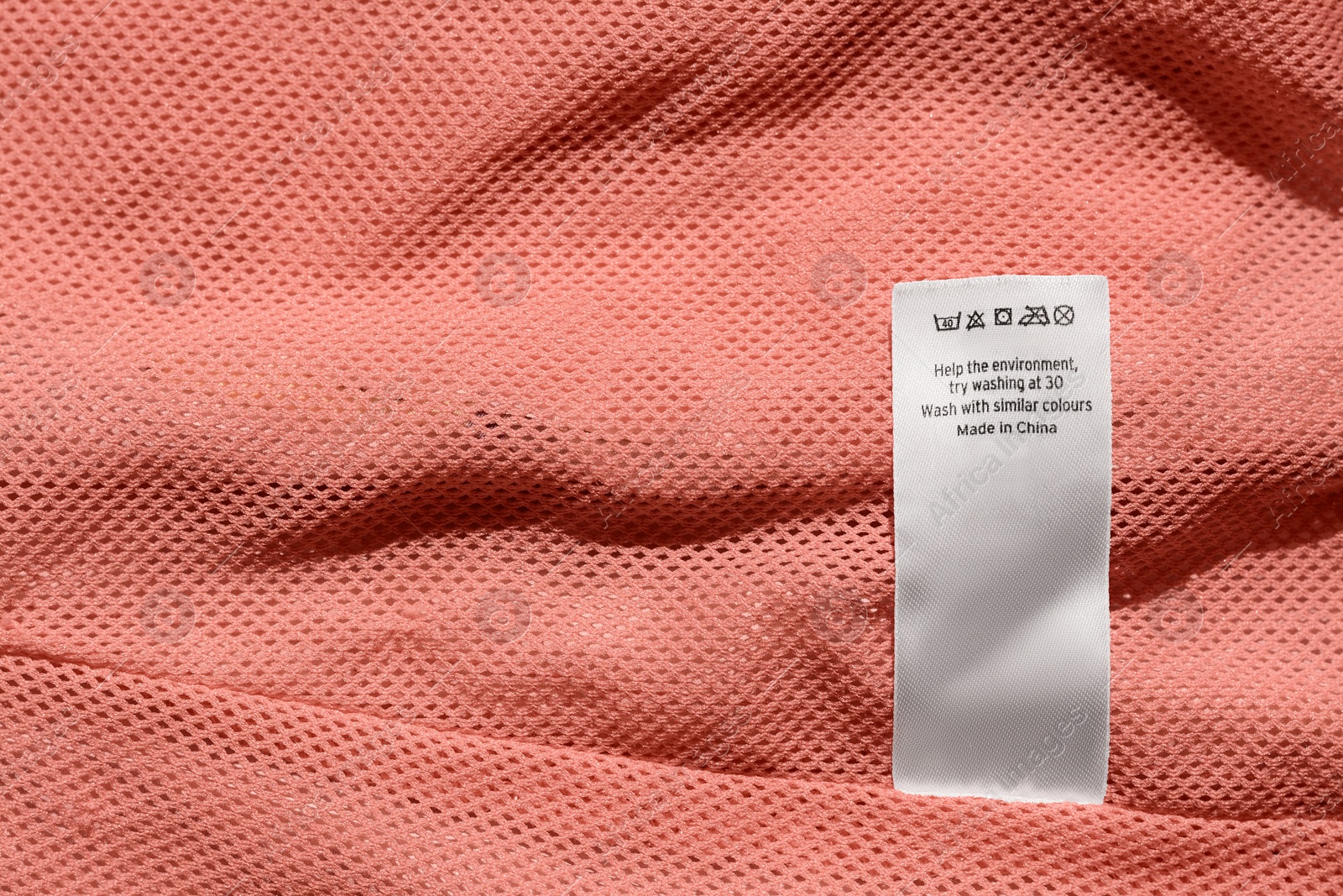 Photo of Clothing label on pink garment, top view. Space for text