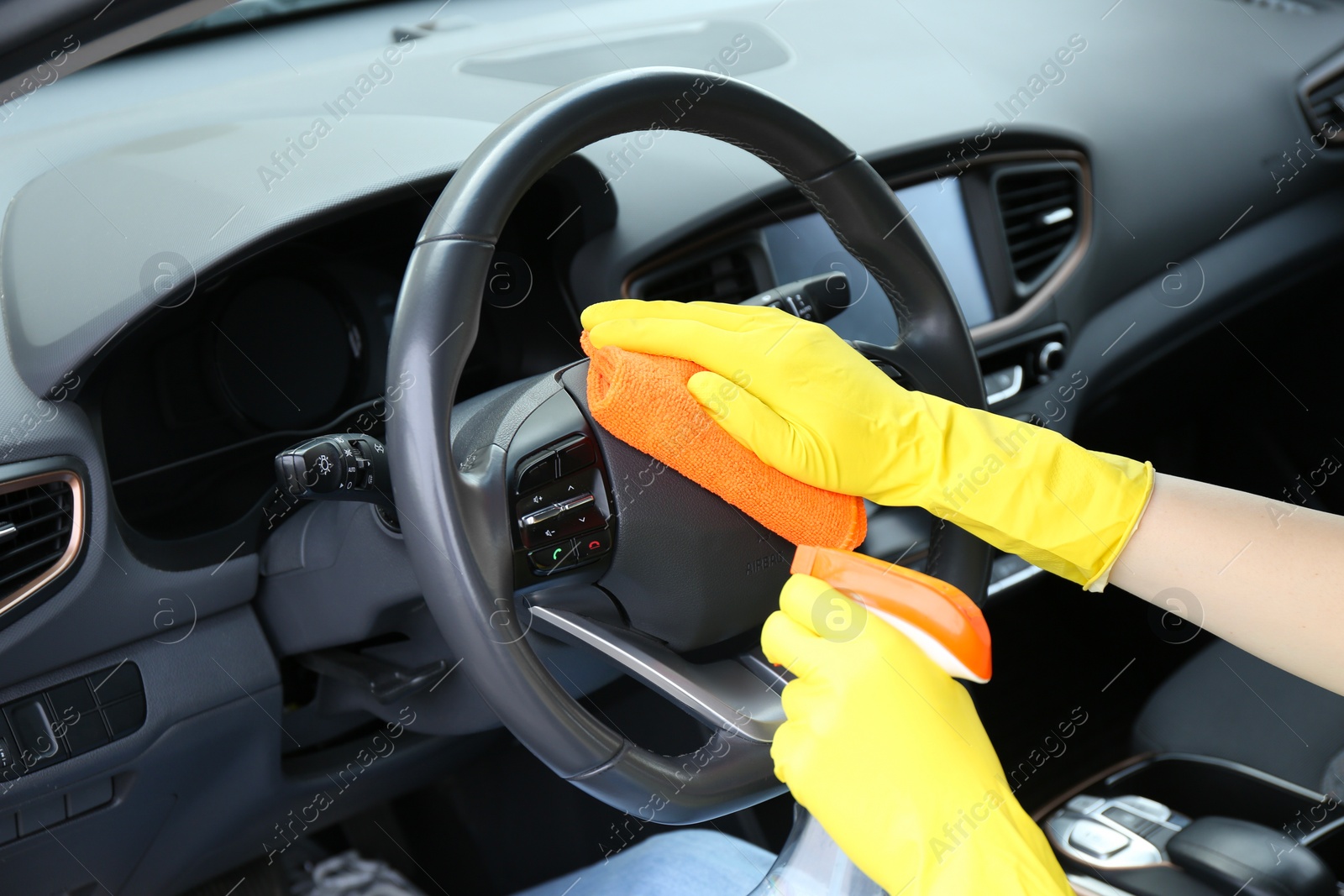 Photo of Woman cleaning steering wheel with rag in car, closeup