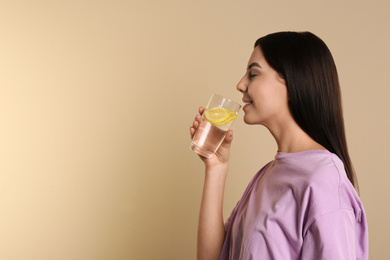 Beautiful young woman drinking tasty lemon water on beige background. Space for text