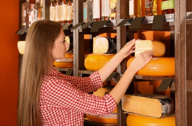 Woman choosing tasty cheese from display in store