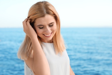 Portrait of beautiful blonde woman near sea, space for text