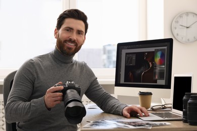Photo of Professional photographer with digital camera using laptop at table in office