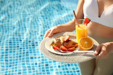 Photo of Young woman with delicious breakfast on tray in swimming pool, closeup. Space for text