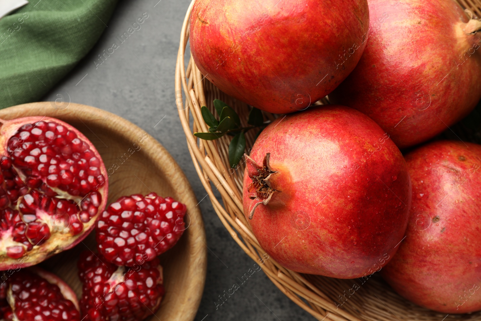 Photo of Fresh pomegranates and green leaves on grey table, top view