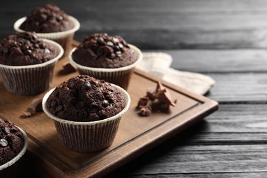 Photo of Delicious chocolate muffins on black wooden table, closeup. Space for text