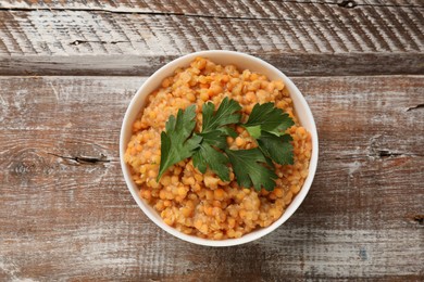 Photo of Delicious red lentils with parsley in bowl on wooden table, top view