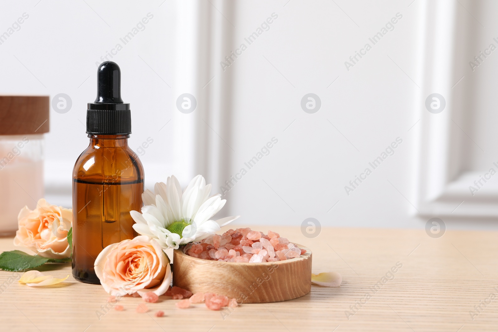 Photo of Bottle of cosmetic serum, sea salt and flowers on wooden table, closeup. Space for text