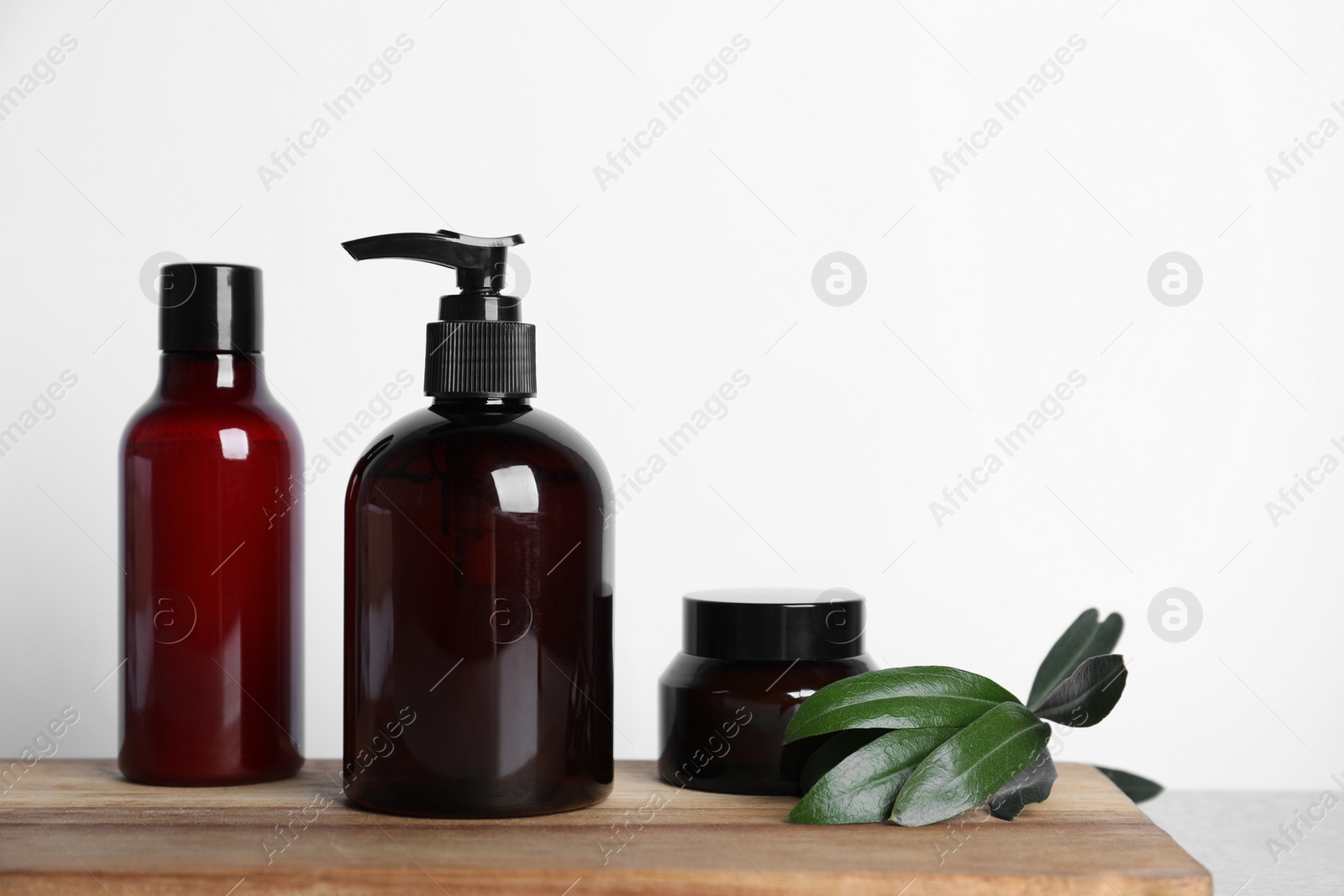 Photo of Different cosmetic products and leaves on wooden board. Space for text