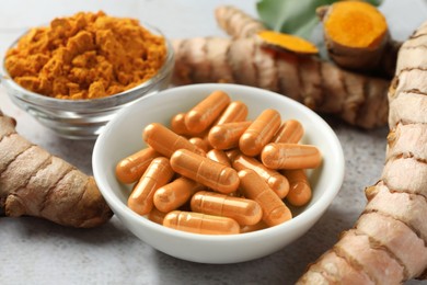 Photo of Turmeric roots, pills and powder on light tiled table, closeup