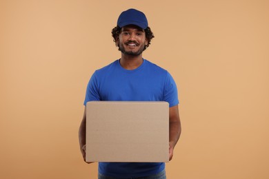 Photo of Happy young courier with parcel on light brown background