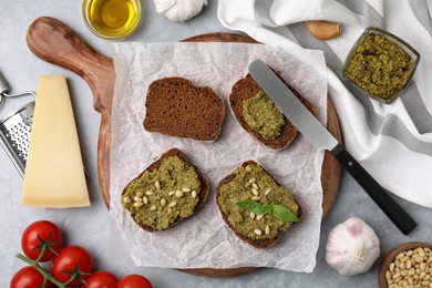 Photo of Making delicious bruschettas with pesto sauce, nuts and fresh basil on light grey table, flat lay