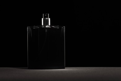 Luxury men`s perfume in bottle on grey table against black background, space for text