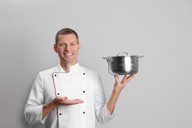 Happy male chef with cooking pot on light grey background