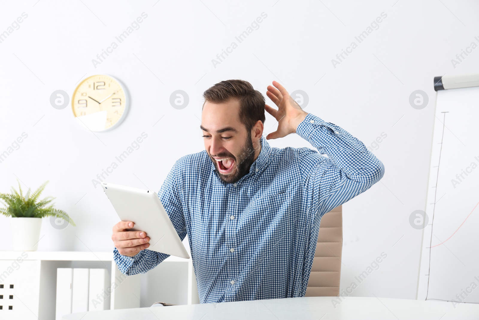 Photo of Emotional young man with tablet celebrating victory in office