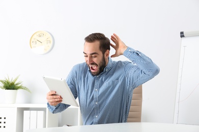 Emotional young man with tablet celebrating victory in office