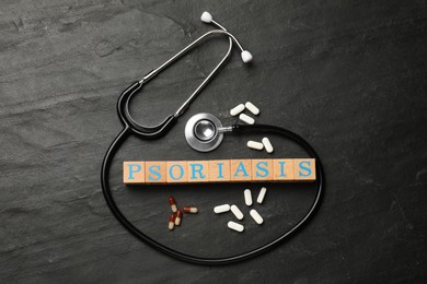 Photo of Word Psoriasis made of wooden cubes with letters, stethoscope and pills on dark gray textured table, flat lay