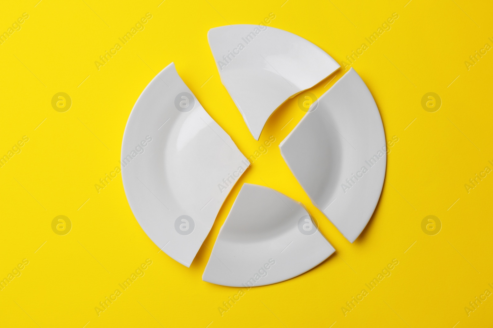 Photo of Pieces of broken white ceramic plate on yellow background, top view. Space for text
