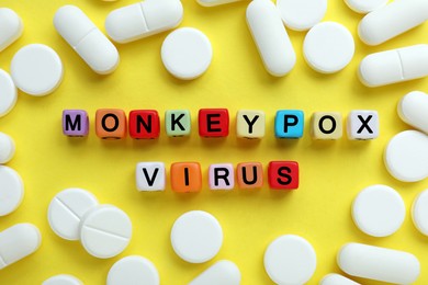 Words Monkeypox Virus made of colorful plastic beads and pills on yellow background, flat lay