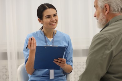Photo of Smiling nurse with clipboard and elderly patient indoors