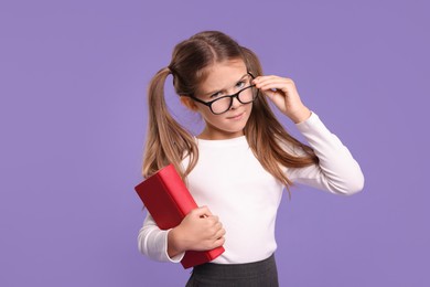 Photo of Cute schoolgirl with book on violet background