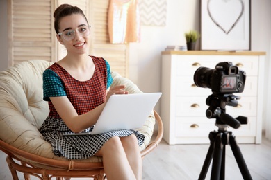 Young blogger with laptop in lounge chair recording video at home