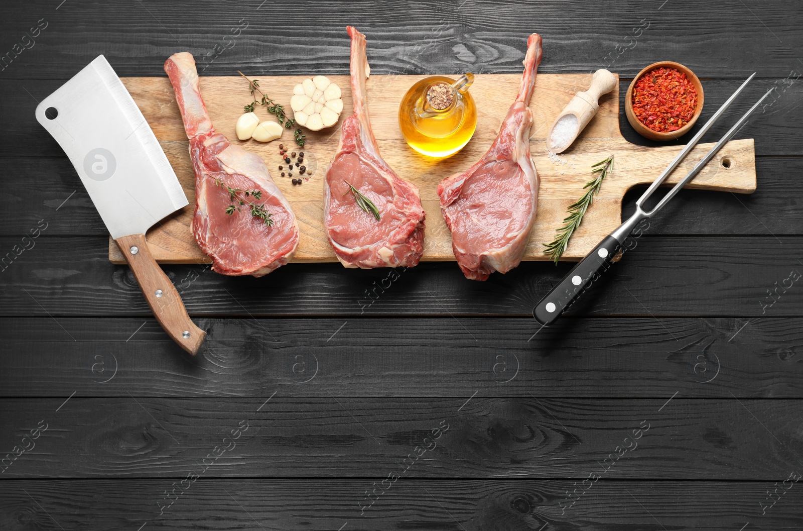 Photo of Fresh tomahawk beef cuts, spices and butcher tools on black wooden table, top view. Space for text