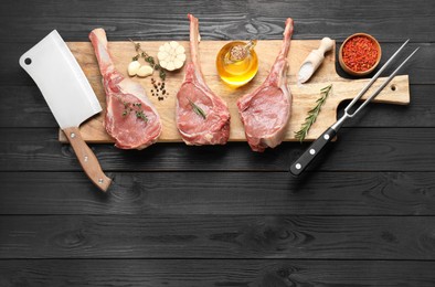 Photo of Fresh tomahawk beef cuts, spices and butcher tools on black wooden table, top view. Space for text