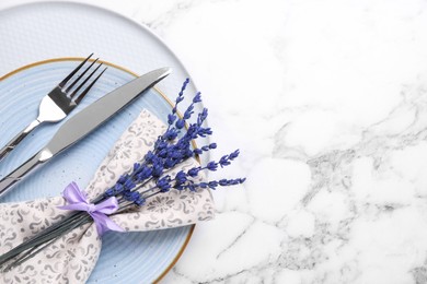 Photo of Cutlery, napkin, plates and preserved lavender flowers on white marble table, top view. Space for text