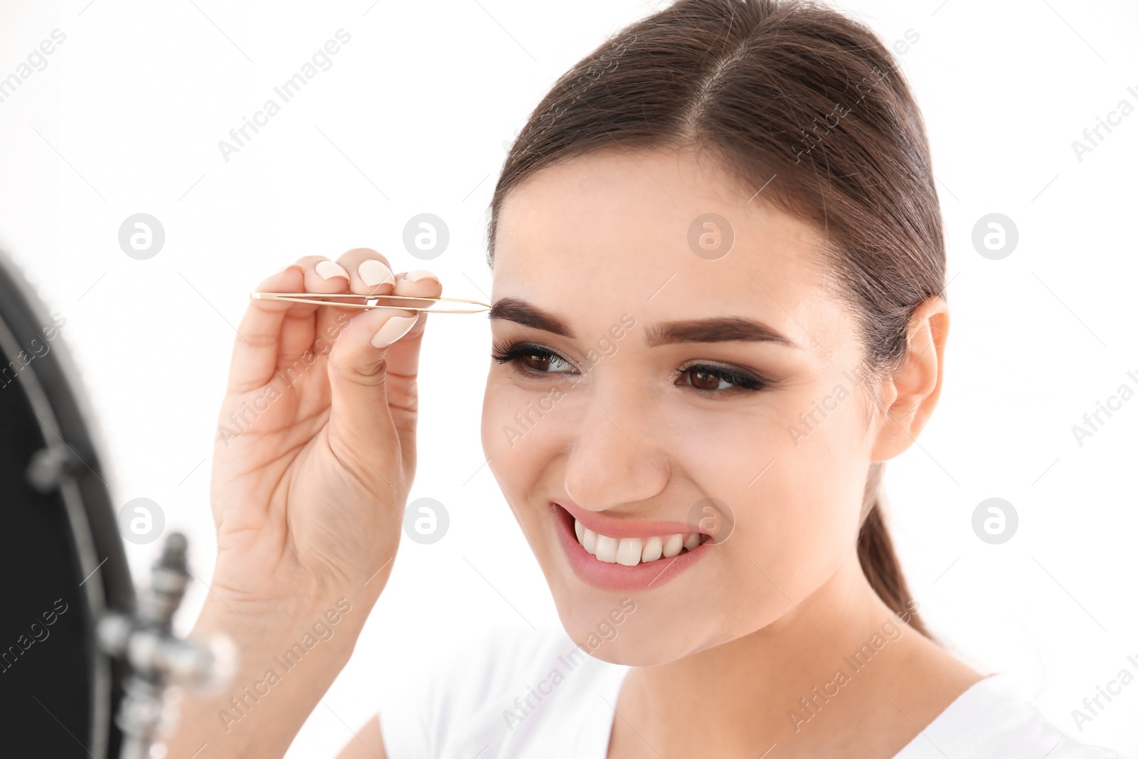 Photo of Young woman plucking eyebrow with tweezers, indoors