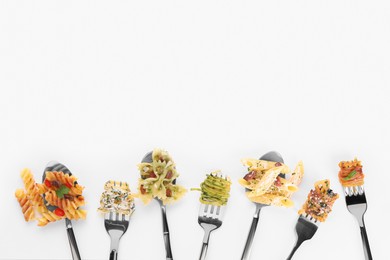 Photo of Forks and spoons with various tasty pasta on white background, flat lay. Space for text