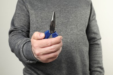 Man with needle nose pliers on light background, closeup. Space for text