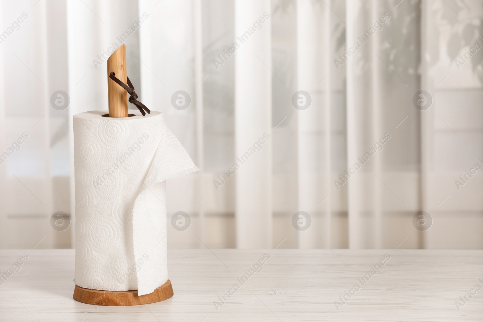 Photo of Holder with roll of paper towels on white wooden table indoors. Space for text