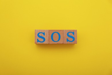Photo of Abbreviation SOS made of wooden cubes on yellow background, top view