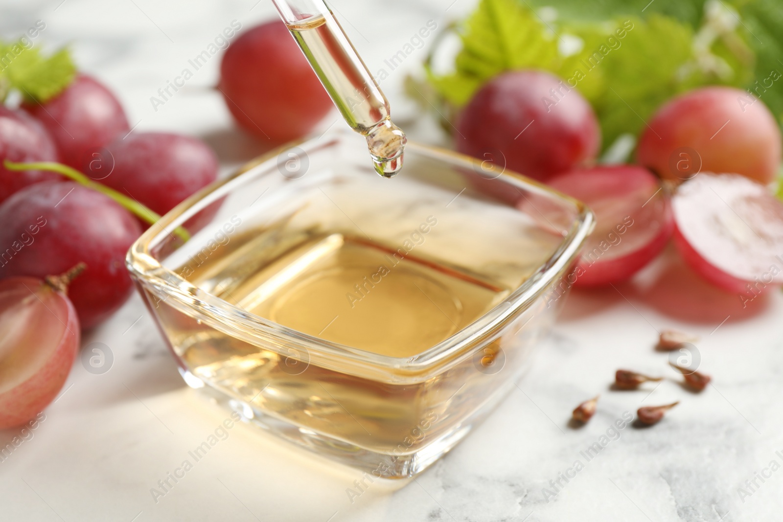 Photo of Dripping natural grape seed oil into bowl on marble table. Organic cosmetic