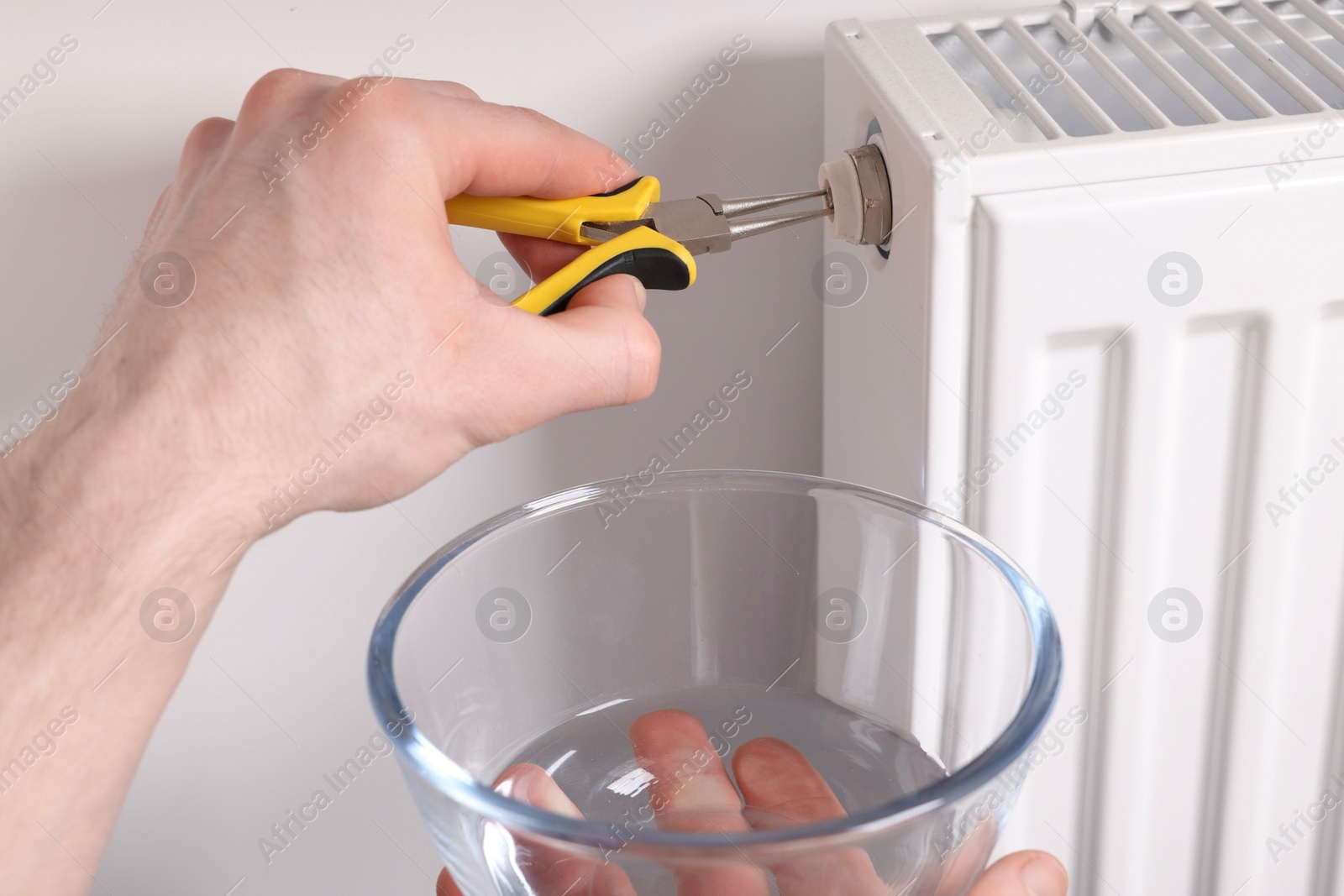 Photo of Professional repairman fixing heating radiator with pliers indoors, closeup