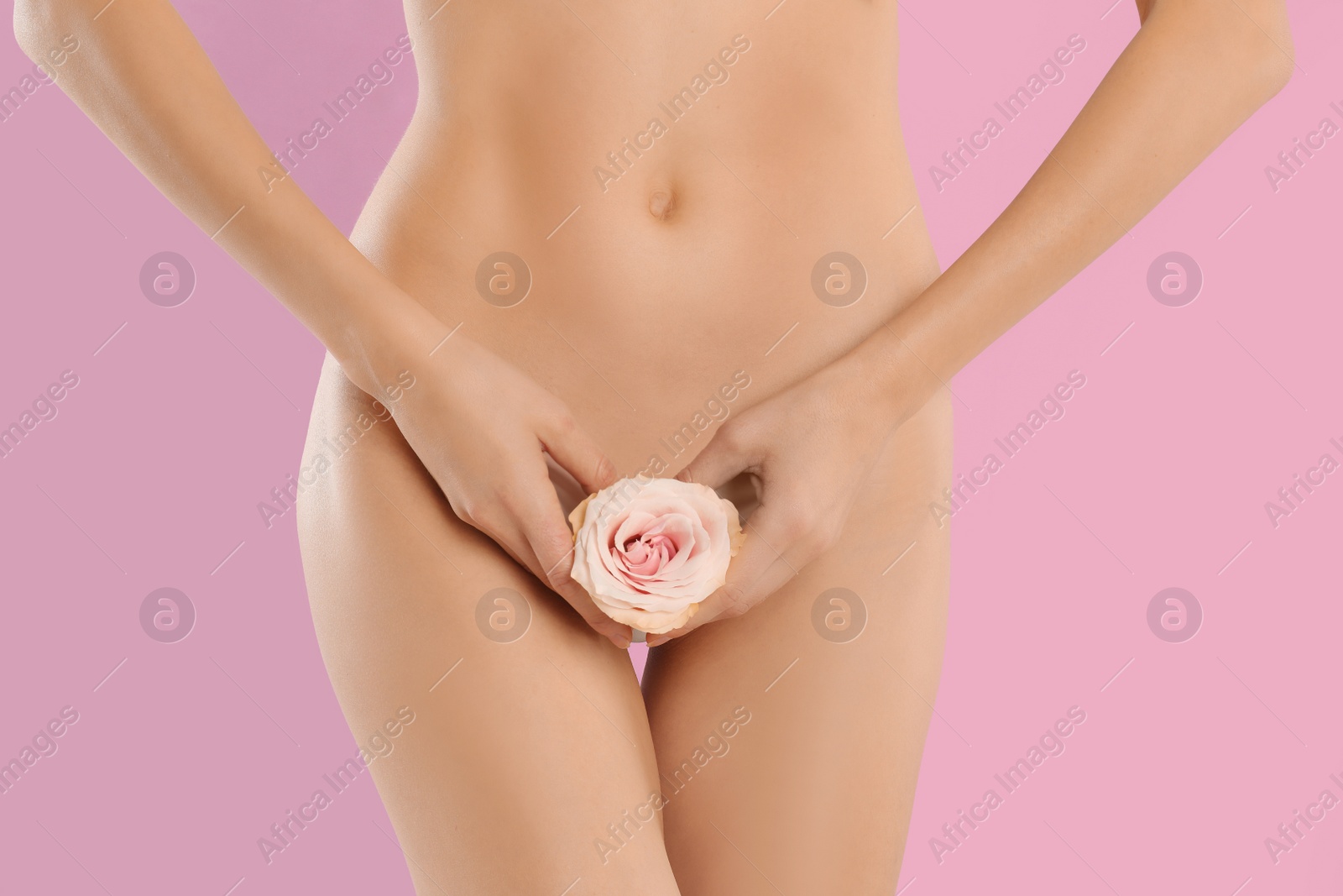 Photo of Woman with flower showing smooth skin after Brazilian bikini epilation on pink background, closeup. Body care concept