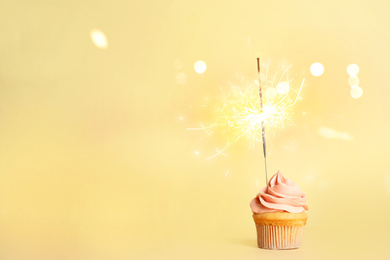 Image of Birthday cupcake with sparkler on light yellow background. Space for text