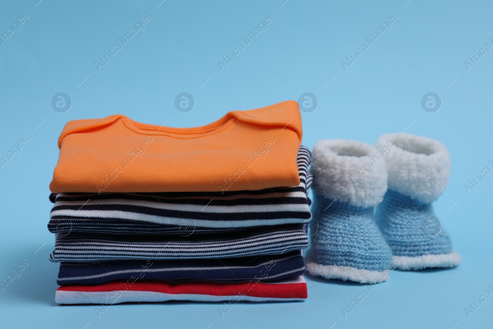 Photo of Stack of clean baby clothes and small booties on light blue background