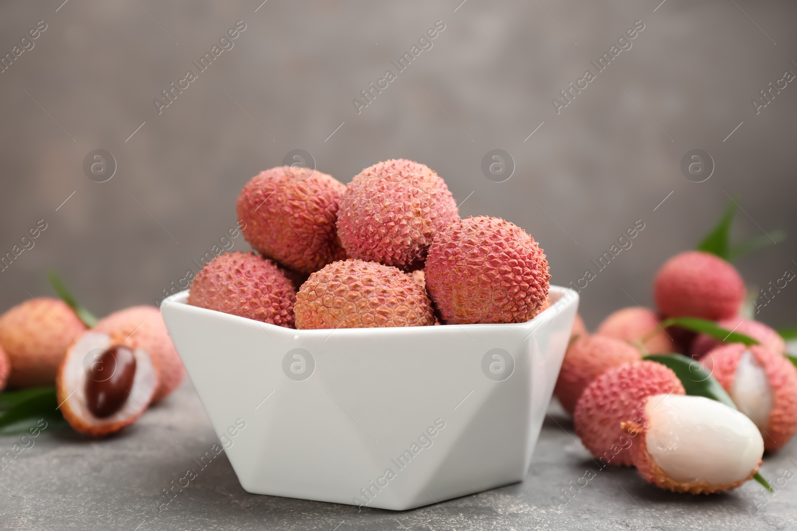 Photo of Fresh ripe lychee fruits in white ceramic bowl on grey table