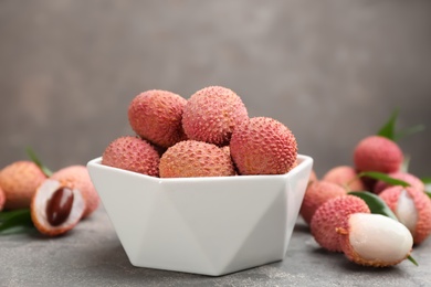 Photo of Fresh ripe lychee fruits in white ceramic bowl on grey table