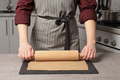 Photo of Woman rolling dough with wooden pin at table in kitchen, closeup