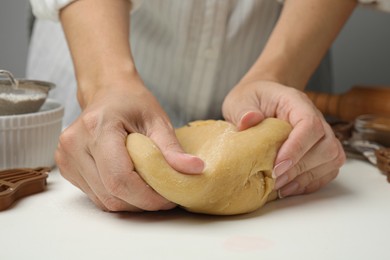 Photo of Woman kneading dough for cookies at white table, closeup