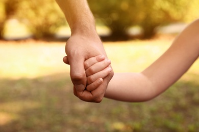 Photo of Little child and father holding hands outdoors, closeup. Family weekend