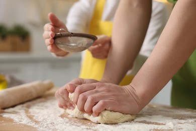 Making bread. Mother and her daughter kneading dough at wooden table in kitchen, closeup