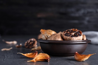 Photo of Bowl with aged black garlic on table. Space for text