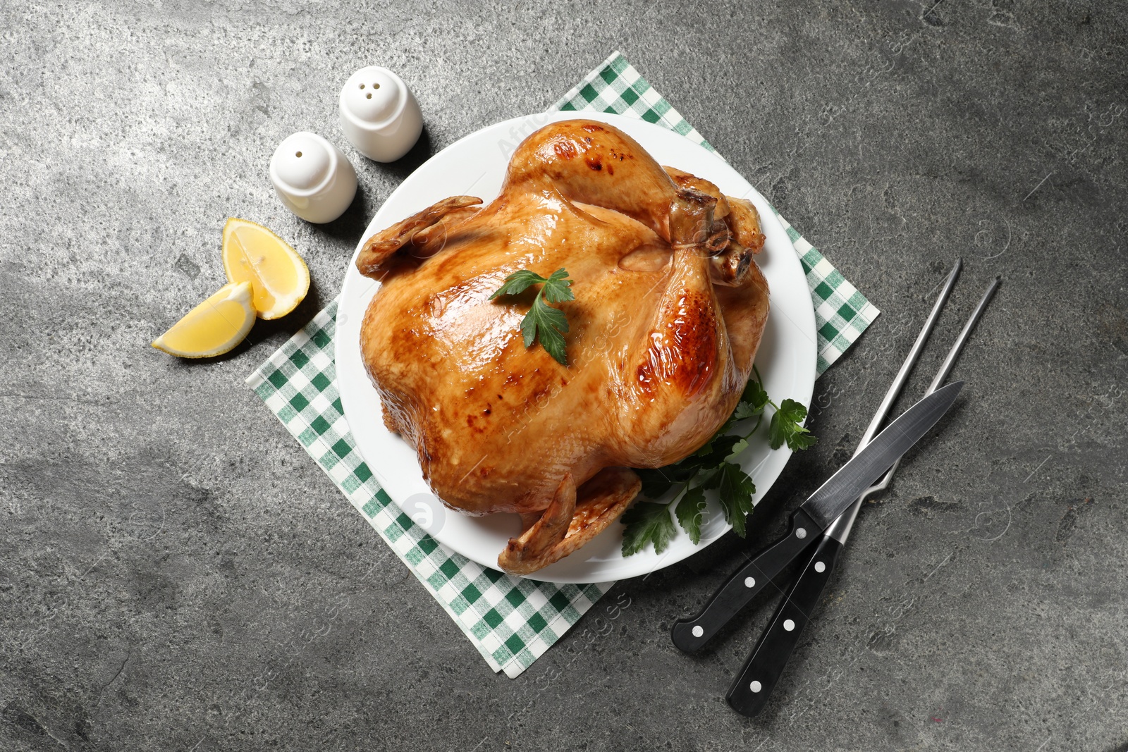 Photo of Tasty roasted chicken with parsley served on grey textured table, flat lay