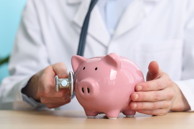 Photo of Doctor with piggy bank and stethoscope at wooden table, closeup