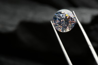 Photo of Tweezers with beautiful shiny diamond on dark background, closeup. Space for text