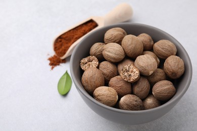 Nutmegs in bowl and scoop with powder on light table, closeup. Space for text